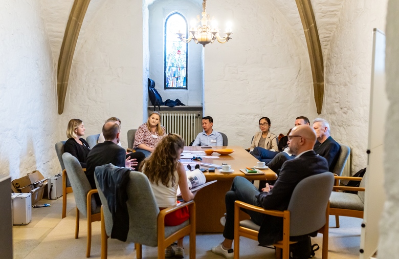 Several people in discussion around a table in a church-like room.